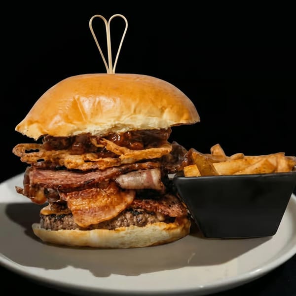 Gourmet burger with bacon, onion rings, and BBQ sauce, served with a side of fries.