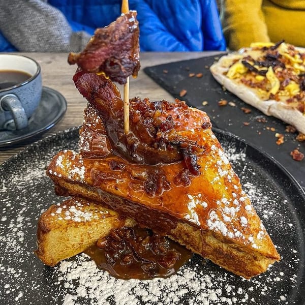 French toast with bacon, caramelized onions, and powdered sugar, served with coffee.