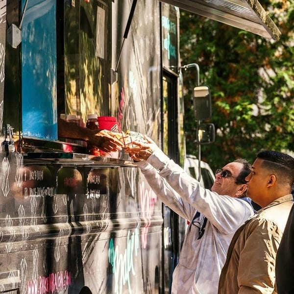 A customer in sunglasses receives food from a food truck vendor on a sunny day.